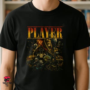 Pode incluir: Uma t-shirt preta de manga curta com uma impressão gráfica que apresenta a palavra PLAYER em letras amarelas grandes no topo. O design inclui uma ilustração detalhada de várias personagens de fantasia e ficção científica, planetas e elementos cósmicos em tons de laranja, dourado e escuro.
