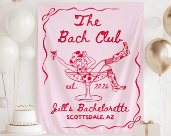 May include: Pink banner with red text and illustration. The text reads "The Bach Club est. 2026" and "Jill's Bachelorette Scottsdale, AZ". The illustration depicts a woman in a cocktail glass wearing a cowboy hat and boots. White balloons and a cake are in the background.