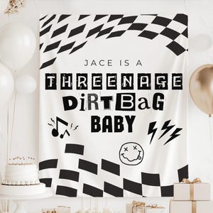 Peut inclure: Une bannière blanche avec des motifs à carreaux noirs et le texte "Jace is a Teenage Dirtbag Baby". La bannière comprend des notes de musique, des éclairs et un smiley. Des ballons blancs et dorés et un gâteau sont en arrière-plan.