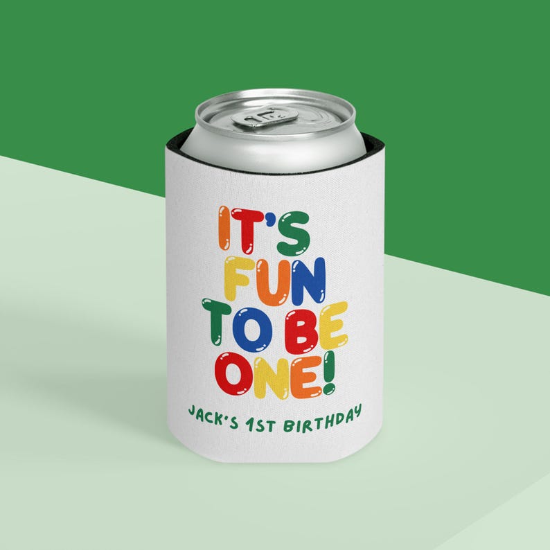 May include: White can cooler with the text "IT'S FUN TO BE ONE!" in colorful bubble letters. The text "JACK'S 1ST BIRTHDAY" is printed below. The cooler is designed to keep beverages cold.