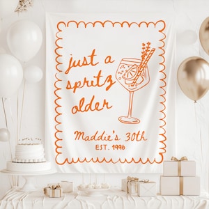 May include: White banner with orange text and illustration for a 30th birthday. The banner reads "just a spritz older" with a cocktail illustration and "Maddie's 30th EST. 1996". The scene includes balloons, a cake, and gifts.