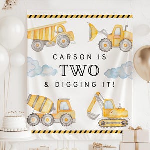 May include: A white banner with watercolor illustrations of construction vehicles, including a dump truck, excavator, and cement mixer. The text "CARSON IS TWO & DIGGING IT!" is displayed in black. Yellow and black stripes border the top and bottom.