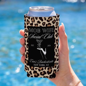 May include: A leopard print can cooler with the text "MOB WIFE Social Club" and a cocktail graphic. The bottom of the cooler reads "Erin's Bachelorette NEW YORK, NY". The cooler is holding a silver can.