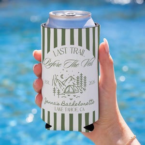 Peut inclure: Un refroidisseur de canette à rayures blanches et vertes avec le texte "LAST TRAIL Before The Veil" et "Jenna's Bachelorette LAKE TAHOE, CA" imprimé dessus. Le design comprend une illustration de montagne, de tente et d'arbres. Le refroidisseur contient une canette argentée.