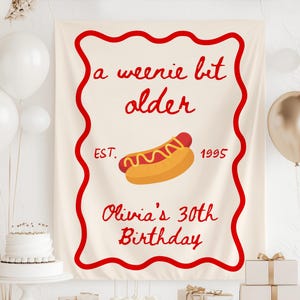 May include: A cream-colored birthday banner with a red border and text that reads "a weenie bit older" with a hot dog graphic. The banner also includes "EST. 1995" and "Olivia's 30th Birthday".