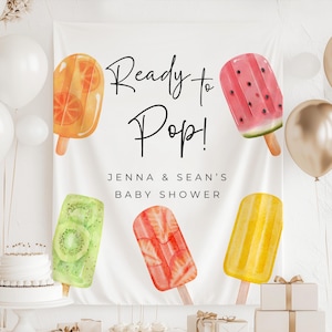 May include: A white banner with the text "Ready to Pop!" and "Jenna & Sean's Baby Shower." The banner features watercolor illustrations of fruit popsicles, including orange, watermelon, kiwi, strawberry, and lemon. Balloons and a small cake are also visible.