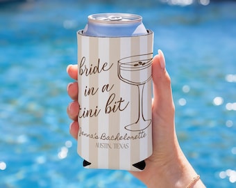 Puede incluir: Un enfriador de latas a rayas beige y blanco con el texto "bride in a tini bit" y una ilustración de copa de martini. También es visible el texto "Jenna's Bachelorette AUSTIN, TEXAS". El enfriador sostiene una lata plateada.