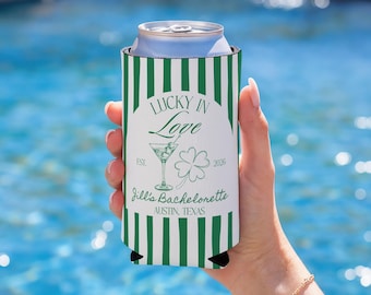May include: A white and green striped can cooler with the text "Lucky in Love" and "Jill's Bachelorette Austin, Texas". The design includes a martini glass and a four-leaf clover. The can cooler is holding a silver can.