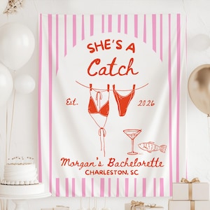 May include: A white banner with pink vertical stripes and the text "SHE'S A Catch" in red. The banner includes illustrations of a bikini, a cocktail, and a fish. The text "Morgan's Bachelorette Charleston, SC" is also present.