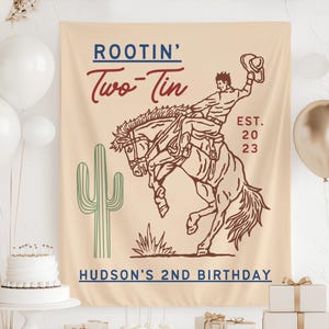 Puede incluir: Una pancarta beige con un vaquero montando un caballo salvaje, con el texto "ROOTIN' Two-Tin" en rojo y azul. Un cactus verde está a la izquierda. El texto "HUDSON'S 2ND BIRTHDAY" está en la parte inferior. Globos y pastel en el fondo.