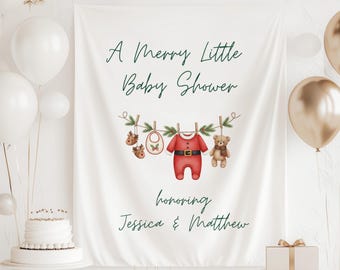 May include: A white banner with the text "A Merry Little Baby Shower" in green script. Below, illustrations of baby clothes and a teddy bear hang from a washing line. The banner also includes the names "Jessica & Matthew".