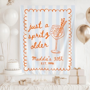 May include: A light blue and white striped banner with orange text that reads "just a spritz older" and "Maddie's 30th EST. 1996". The banner has an orange border and a drawing of a cocktail.