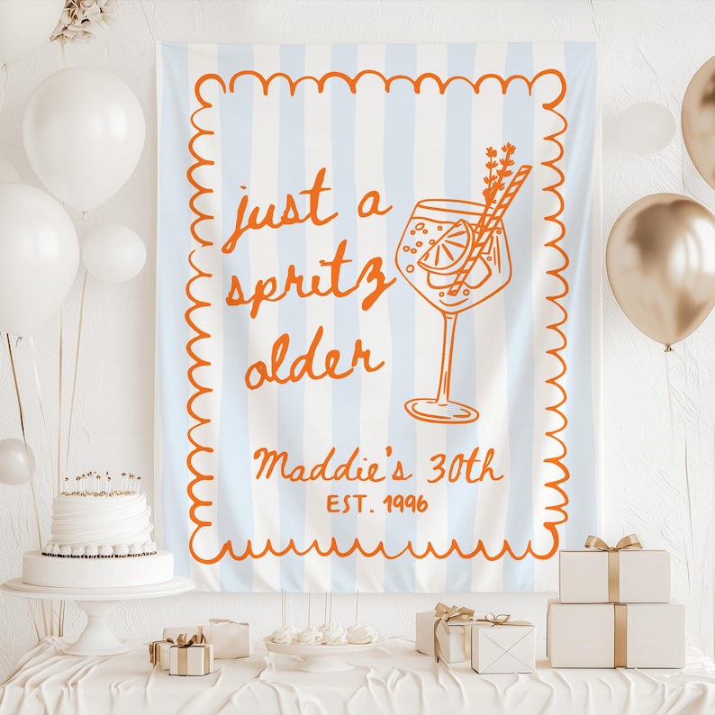 May include: A light blue and white striped banner with orange text that reads "just a spritz older" and "Maddie's 30th EST. 1996". The banner has an orange border and a drawing of a cocktail.