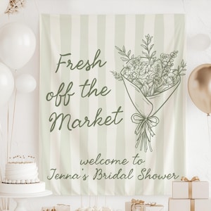 Puede incluir: Una pancarta con el texto "Fresh off the Market" y una ilustración de un ramo de flores. La pancarta tiene un fondo a rayas e incluye el texto "welcome to Jenna's Bridal Shower". Se ven globos blancos y dorados.