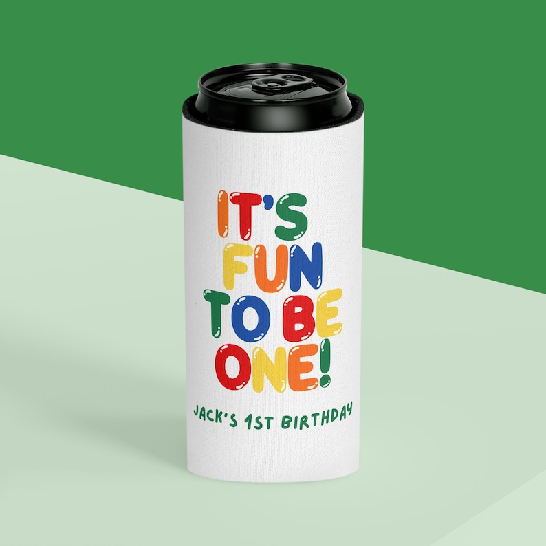 May include: A white can cooler with a black top. The text "IT'S FUN TO BE ONE!" is printed in colorful letters. Below the text is "Jack's 1st Birthday" in green.