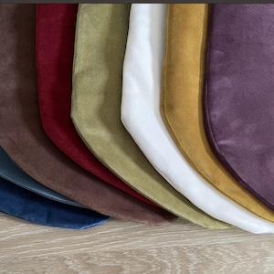 Puede incluir: Una colección de calcetines navideños de terciopelo en varios colores, incluyendo azul, marrón, rojo, verde, blanco, dorado y morado. Los calcetines están dispuestos en forma de abanico, mostrando su textura suave y ricos tonos.