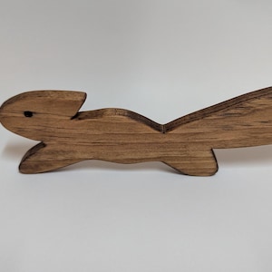 May include: A wooden squirrel ornament, crafted from light brown wood. The squirrel is shown in a running position, with a long, curved tail and small, pointed ears. The wood grain is visible.