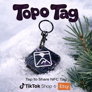 May include: A square Topo Tag keychain with a black clasp and ring. The tag has a purple and black marbled design with a white mountain graphic. The words "Topo Tag" are in purple script above the tag. The text "Tap to Share NFC Tag" is below the tag.