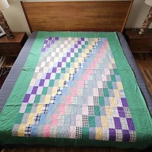 May include: A handmade quilt with a patchwork design in various colors, including green, purple, pink, and yellow. The quilt is laid out on a bed with a wooden headboard and nightstands. The quilt's dimensions are approximately 80 inches by 90 inches.