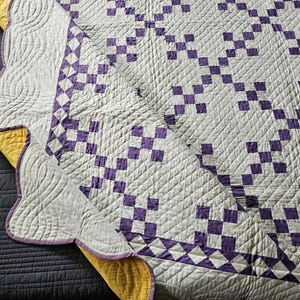 May include: A handmade quilt with a white background and a repeating pattern of purple squares. The quilt has a scalloped edge with a purple border and yellow backing. The quilting creates a textured surface.