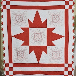 May include: A handmade quilt with a central red star design and four floral motifs on a white background. The quilt features red and white striped borders and a decorative zigzag edge. The dimensions are approximately 70 inches by 80 inches.