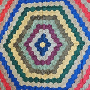 May include: A vintage quilt with a repeating hexagonal pattern in a variety of colours. The quilt features concentric rings of red, blue, green, yellow, and purple. The design creates a visually striking, geometric effect, suitable for home decor.