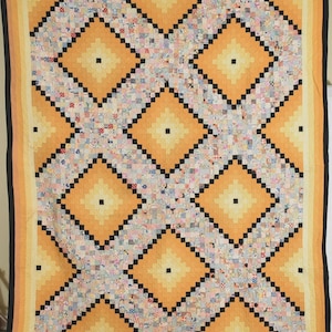 Könnte beinhalten: Eine rechteckige Steppdecke mit einem sich wiederholenden Rautenmuster in Orange- und Gelbtönen. Das Design besteht aus kleinen, mehrfarbig gemusterten Stoffquadraten, die von dünnen schwarzen Linien umrandet sind und ein geometrisches Gitter bilden.
