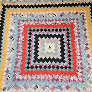 May include: Handmade quilt with a vibrant, geometric design. The quilt features a central square of black and white zigzags, surrounded by red, pink, and blue squares. The outer edges have alternating black, yellow, and blue stripes. A cozy, colourful textile.