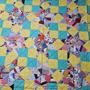 Könnte beinhalten: Ein Patchwork-Quilt mit einem sich wiederholenden Muster aus gelben und türkisfarbenen Quadraten. Der Quilt besteht aus verschiedenen Stoffresten in einer Vielzahl von Farben und Mustern, darunter Blumen-, Streifen- und unifarbene Stoffe. Der Quilt ist handgefertigt.