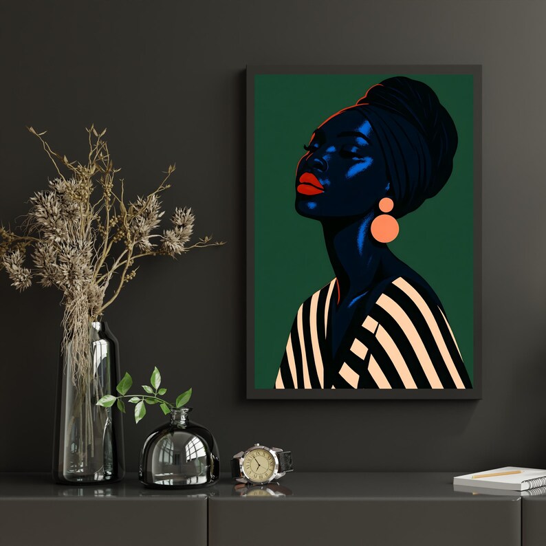 May include: A framed art print featuring a stylized portrait of a woman with dark skin, wearing a black head wrap and orange earrings. She has red lipstick and a striped top against a green background. The artwork is displayed on a dark gray surface.