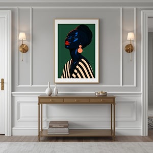 May include: A framed art print featuring a stylized portrait of a person with dark skin, wearing a black head wrap and striped top. The person has red lips and orange earrings, set against a dark green background.
