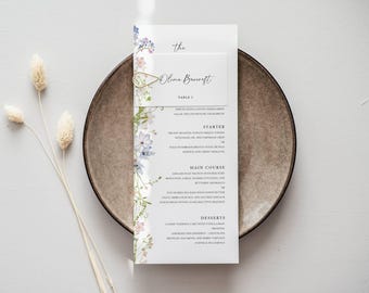 Può includere: Un menu di nozze con dettagli floreali, con il nome "Olivia Braecroft". Il menu è presentato su un piatto marrone, con fiori secchi a sinistra. Il menu elenca antipasti, piatti principali e dessert.