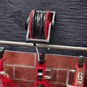 Op de afbeelding: Een set rode en zwarte autokrikken met een capaciteit van 6 ton. Een zwarte en rode haspel is op de muur boven de krikken gemonteerd. De krikken zijn voorzien van het label "CHUBBY JACKSTAND".