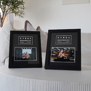 May include: Two black framed photos with the text "HYROX BIRMINGHAM" at the top. One photo shows a couple, the other shows a person in action. The photos are on a white table.