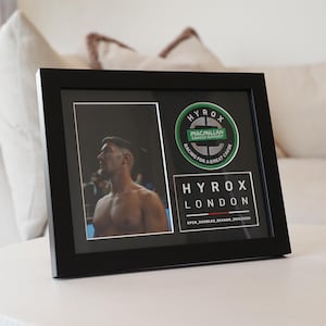 May include: Black framed photo with a man's image and HYROX logo. The HYROX logo includes the text "MACMILLAN CANCER SUPPORT" and "RACING FOR A GREAT CAUSE". The text "HYROX LONDON" and "OPEN DOUBLES SEASON 2025/2026" are also visible.