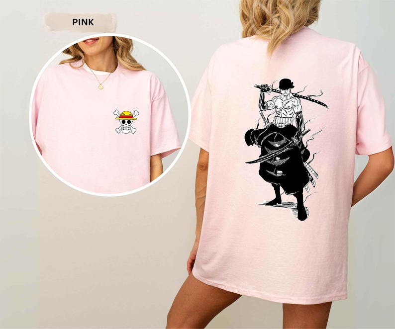 K&ouml;nnte beinhalten: Hellrosa T-Shirt mit einem kleinen Cartoon-Totenkopf und gekreuzten Knochen mit Strohhut auf der Vorderseite. Die R&uuml;ckseite des T-Shirts zeigt eine Schwarz-Wei&szlig;-Illustration einer Figur mit Schwertern.