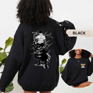 K&ouml;nnte beinhalten: Schwarzes Sweatshirt mit einer wei&szlig;en Grafik eines Charakters mit Schwertern auf dem R&uuml;cken. Das Sweatshirt hat auch eine kleine Grafik eines Totenkopfes und gekreuzten Knochen auf der Vorderseite. Das Wort "BLACK" wird auf dem Bild angezeigt.