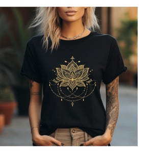 Könnte beinhalten: Schwarzes T-Shirt mit einem goldenen Lotusblumen-Design. Das komplizierte Blumenmuster umfasst detaillierte Blütenblätter, Punkte und hängende perlenartige Akzente. Das Shirt ist ein klassischer Rundhalsausschnitt.