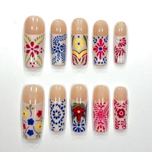 May include: A set of ten artificial nails with a nude base and colorful floral designs. The designs include red, blue, yellow, and white flowers and patterns. The nails are in various sizes and shapes.