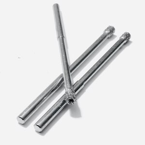 May include: Three silver drill bits with diamond tips. The drill bits are arranged in a criss-cross pattern.
