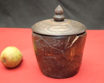 May include: A handcrafted wooden jar with a lid, featuring a dark brown finish and visible wood grain. The jar has a cylindrical shape with a lid and a small knob on top. A pear is next to the jar.
