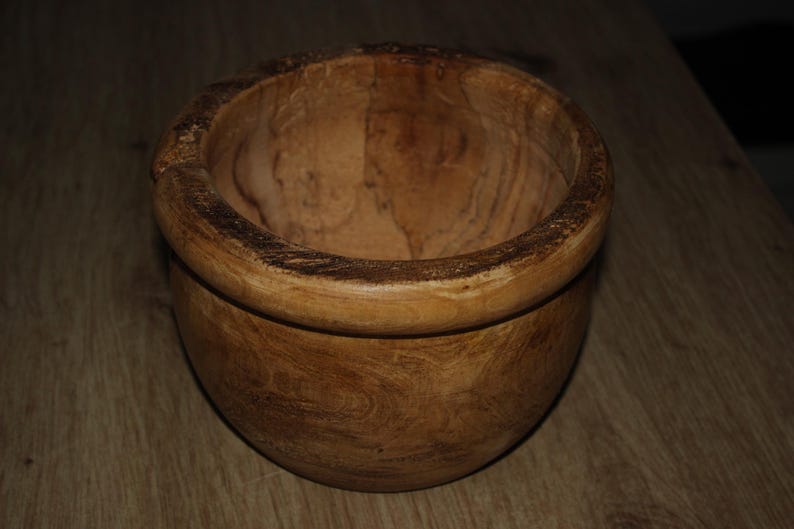 May include: A wooden bowl with a natural finish. The bowl has a rounded shape with a wide rim and a textured surface, showing the wood grain. This decorative bowl is suitable for serving or display, and is a rustic item.