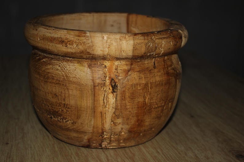May include: A wooden bowl with a rounded body and a thick, rounded rim. The bowl is made of light brown wood with visible grain and knots, suggesting a natural, rustic aesthetic. The bowl is empty.