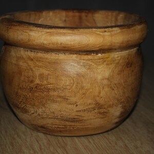 May include: A wooden bowl with a rounded base and a thick, rounded rim. The bowl has a natural wood grain pattern with varying shades of brown and tan. This decorative bowl is suitable for kitchen or home decor.