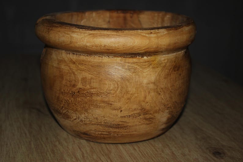 May include: A wooden bowl with a rounded base and a thick, rounded rim. The bowl has a natural wood grain pattern with varying shades of brown and tan. This decorative bowl is suitable for kitchen or home decor.