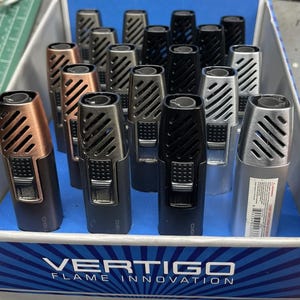 May include: A selection of Vertigo lighters in a range of metallic colours, including copper, silver, and black. The lighters have a rectangular shape with angled vents and a push-button ignition. The box displays the brand name and tagline.