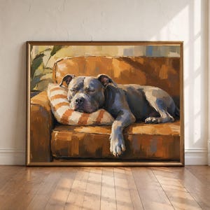 Op de afbeelding: Een ingelijst olieverfschilderij met een grijze hond die slaapt op een bruine leren bank. De hond rust zijn kop op een oranje en wit gestreept kussen. Het kunstwerk toont zichtbare penseelstreken en warme tinten in een rustig tafereel.