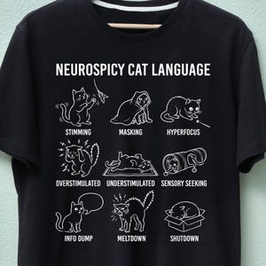 May include: Black t-shirt with the text "NEUROSPICY CAT LANGUAGE" above a series of white cat illustrations depicting various behaviors, including "Stimming," "Masking," and "Hyperfocus."