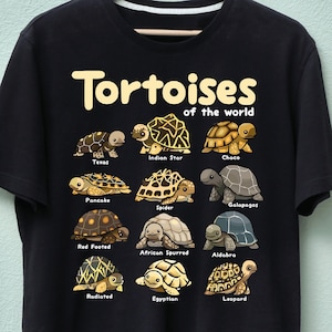 May include: Black t-shirt featuring the text "Tortoises of the World" above illustrations of various tortoise species, including Texas, Indian Star, and Choco. The shirt design includes the names of each tortoise type.
