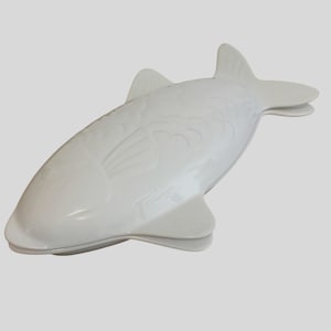 Könnte beinhalten: Eine weiße, fischförmige Servierschale aus Keramik. Die Schale hat eine glänzende Oberfläche und detaillierte Schuppen und Flossen. Das Design ist eine stilisierte Darstellung eines Fisches, geeignet zum Servieren von Vorspeisen oder kleinen Gerichten.